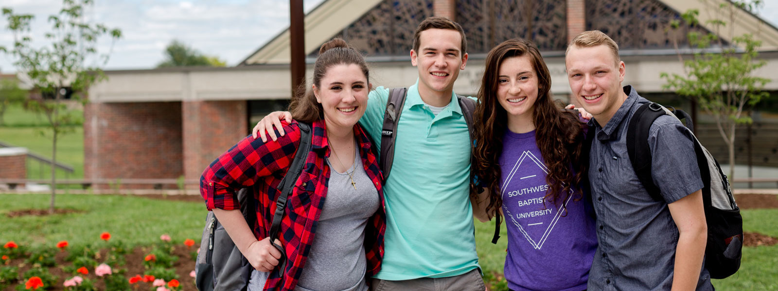 female student holding book in foreground; three students sitting on stairs in background