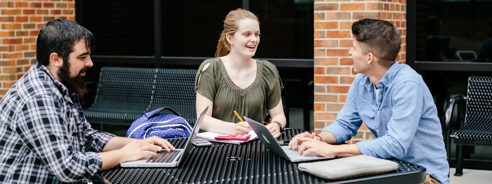 three students working on homework at outside picnic table