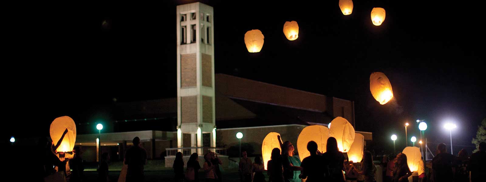 students release lanterns into night sky in front of bell tower