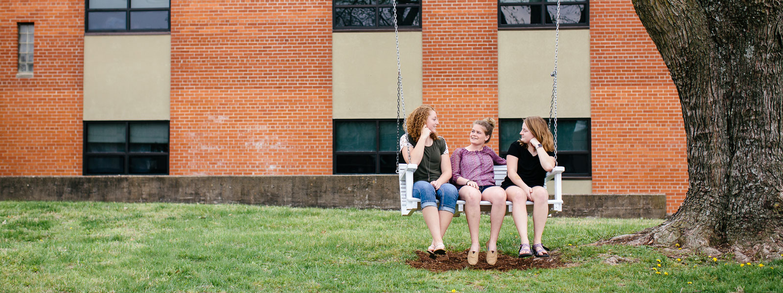 three students sitting on swing outside dorm