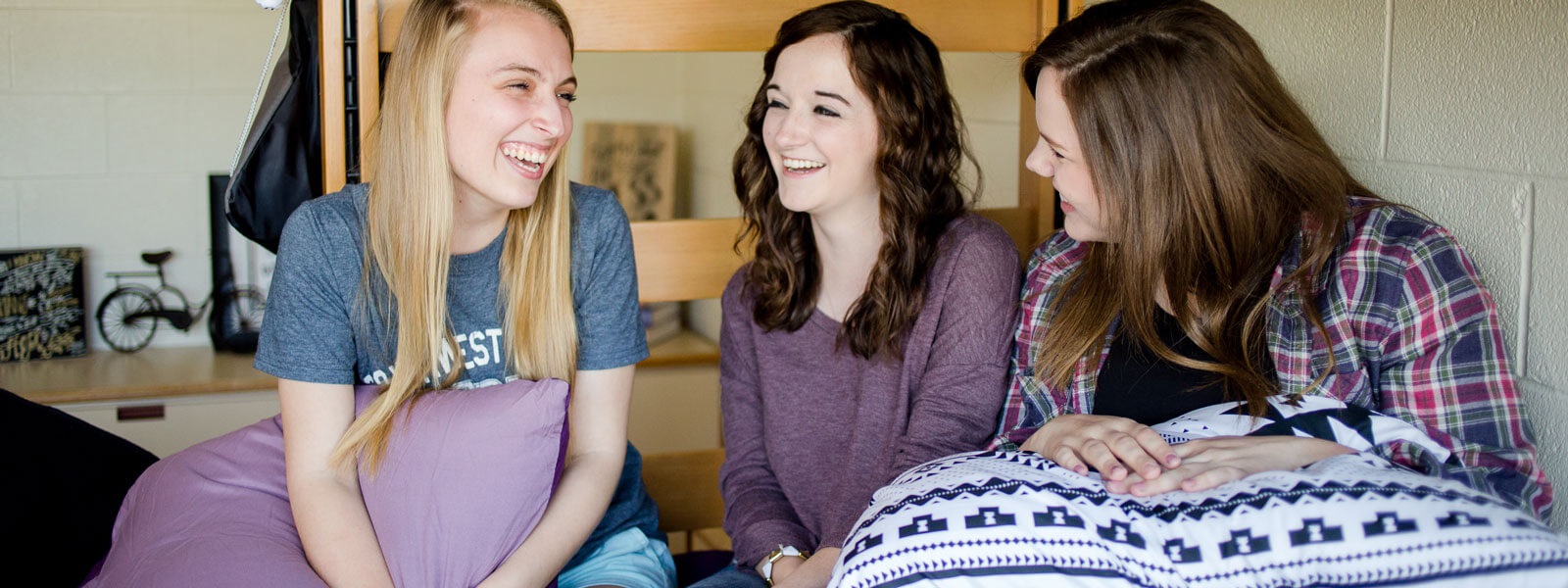 three female students sitting on bunk bed in dorm room