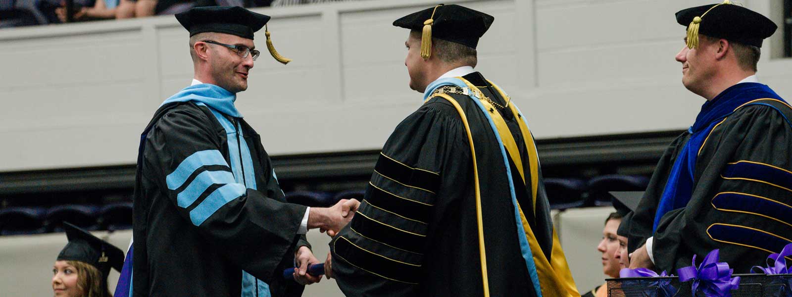 doctor of education graduate shakes president's hand as he receives diploma on graduation stage