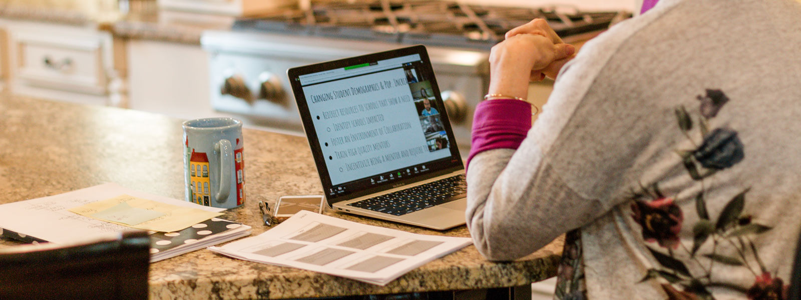 teacher sitting at kitchen table with laptop and coffee mug